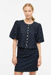 Ensemble en denim comprenant une robe bleu marine à pois bleu clair, manches courtes ballons et détails de boutons métalliques sur le devant.