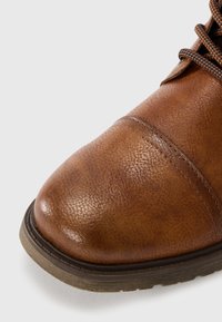 Brun læderstøvle med en struktureret overflade, rund tå, kontrasterende sål og mørke snørebånd, med synlige syninger og et holdbart ydre design.