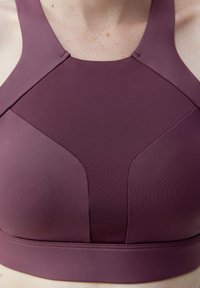 Sportbh i djupt mauve med en åtsittande design. Har breda axelband och sömlös konstruktion som framhäver konturerande paneldetaljer. Mjuk textur.