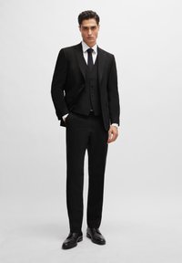 Black three-piece suit featuring a tailored jacket, vest with five buttons, and matching trousers. Crisp white shirt and black tie complete the look.