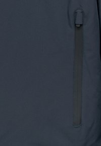 Giacca di tessuto blu navy con una tasca verticale con zip sul lato sinistro, texture liscia e design minimalista.