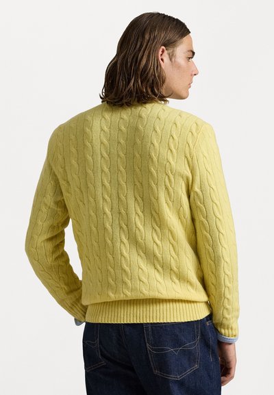 Dzeltena adīta džemperis ar ribotu apakšmalu, kuram ir teksturēts raksts. Aizmugurei ir gluda apdare un apaļa izgriezuma kakla līnija.