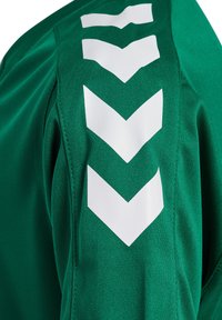Camiseta deportiva verde con patrones en forma de chevron blancos en los hombros. Fabricada con un tejido texturizado y costuras reforzadas para mayor durabilidad.