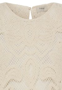 Haut en dentelle crochetée couleur crème avec motifs floraux et feuillage, encolure ronde et fermeture par boutons au dos.