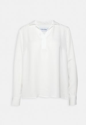 Blusa bianca a maniche lunghe con scollatura a V e colletto, realizzata in tessuto morbido. Presenta polsini con bottone e orlo dritto, design minimalista.