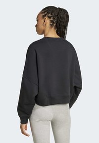 Černá zkrácená mikina s oversized rukávy a kulatým výstřihem, vyrobená z měkké tkaniny, nošena s světle šedými legínami.