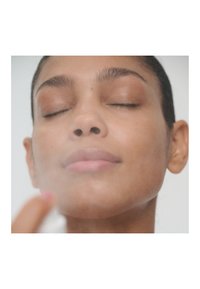 Eine Frau mit geschlossenen Augen, die einen Gesichtsspray verwendet, mit glatter Haut, dezentem, natürlichem Make-up und einem sanften Glanz im Gesicht.
