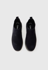 Une paire de mocassins en daim noir avec des tirettes, des bouts ronds et des semelles texturées sombres, vue du dessus sur un fond blanc.