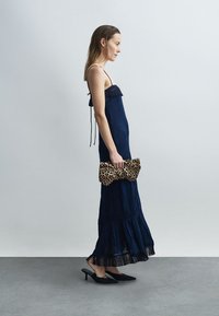 Tamsiai mėlyna, sluoksniuota maksi suknelė su raukšlėtu iškirpimu ir plonomis petnešėlėmis, derinama su leopardų rašto delnine ir juodais smailiais aukštakulniais.