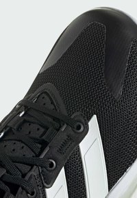 Black athletic shoe featuring a textured mesh upper, flat laces, white accent stripes, and a smooth black toe cap.