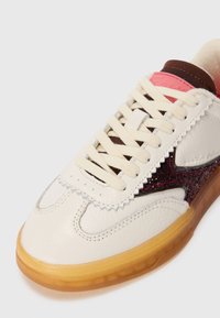Hvit lær sneaker med rosa og brune detaljer. Har en glitrende burgunder panel, kremfargede snørebånd, og teksturert gummisåle. Bølgeformet detalj nær tå.