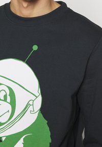 Ciemnogranatowa bluza z dużym, białym i zielonym kreskówkowym małpkiem w hełmie kosmicznym; posiada prążkowany dekolt i miękką teksturę.