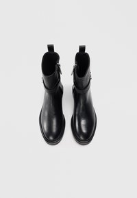 Bottines noires en cuir avec une texture lisse, bout rond et fermeture éclair sur le côté. Présente une languette à l'arrière pour un enfilage facile.