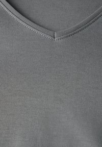 Tessuto grigio con una superficie liscia e un design a V. Presenta una cucitura piatta attorno al collo e una maglia uniforme e costante in tutto il capo.