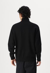 Maglione nero con colletto alto, realizzato in un tessuto morbido. Presenta maniche lunghe e un orlo aderente, evidenziando un design minimalista.