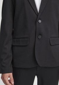 Black blazer with two buttons, notched lapel, and side pockets. Made from a smooth, matte fabric, featuring a fitted design.