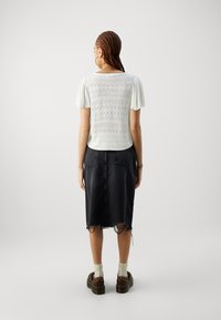 Witte T-shirt met korte mouwen en een textuur gebreid patroon, gecombineerd met een zwarte spijkerrok tot de knie, met franje aan de onderkant en twee achterzakken.