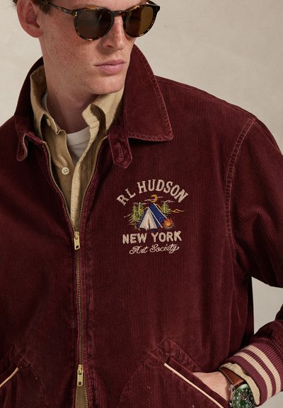 Bordeauxrode corduroy jas met ritssluiting, geborduurd kampterrein en tekst "RL Hudson New York Art Society". Voorzien van omgeslagen boorden en zakken.