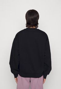 Sudadera negra de corte holgado, con mangas ribeteadas y un cuello redondo. Textura suave, sin logotipos ni patrones visibles.