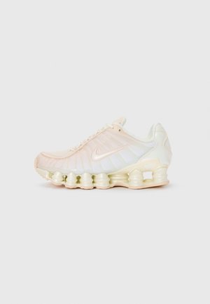 Beżowo-białe buty sportowe Nike z widoczną sprężynową amortyzacją podeszwy i cholewką z siateczki z wiązaniem na sznurówki.