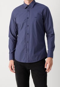 Mörkblå knapp-up skjorta i lätt material med en subtil lyster. Den har krage, långa ärmar och en liten logotyp på bröstet.