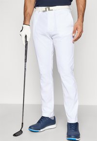 Λευκά παντελόνια γκολφ με υφή, συνδυασμένα με μπλε πουκάμισο και ναυτικές γκολφ παπουτσιές. Μια λευκή ζώνη ολοκληρώνει την εμφάνιση. Φοράει γάντια στο αριστερό χέρι.