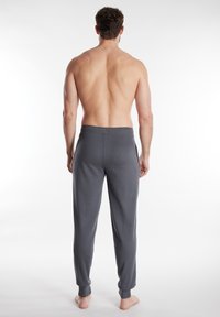 Pantaloni lounge grigi realizzati in un tessuto morbido, con una vestibilità ampia, vita elastica e caviglie a sbuffo, visti da dietro.