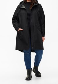 Black waterproof coat with a zip front, hood, and side pockets. Made of smooth material; features minimalist design and relaxed fit.