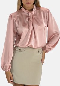 Rosa Satinbluse mit hohem Ausschnitt und gerafften langen Ärmeln, kombiniert mit einem beigen Minirock mit Knopfdetails.