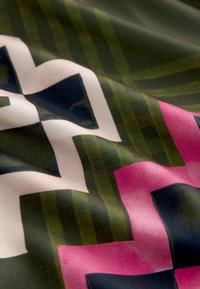 Geometriai mintás szövet zöld csíkokkal, rózsaszín és fehér szögletes alakzatokkal, sima, kissé gyűrött felületen.