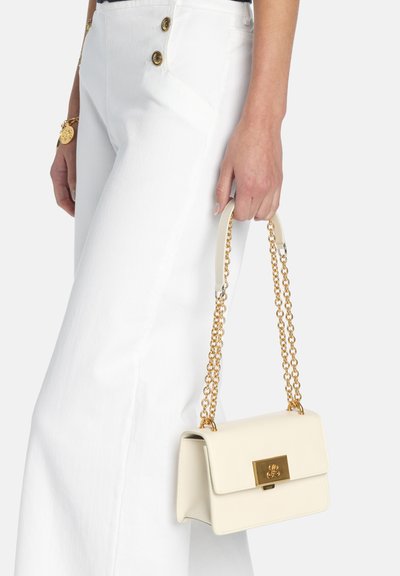 Sac à main en cuir crème avec une forme structurée, une quincaillerie dorée et une bandoulière en chaîne. Il possède une fermeture magnétique et une texture lisse.