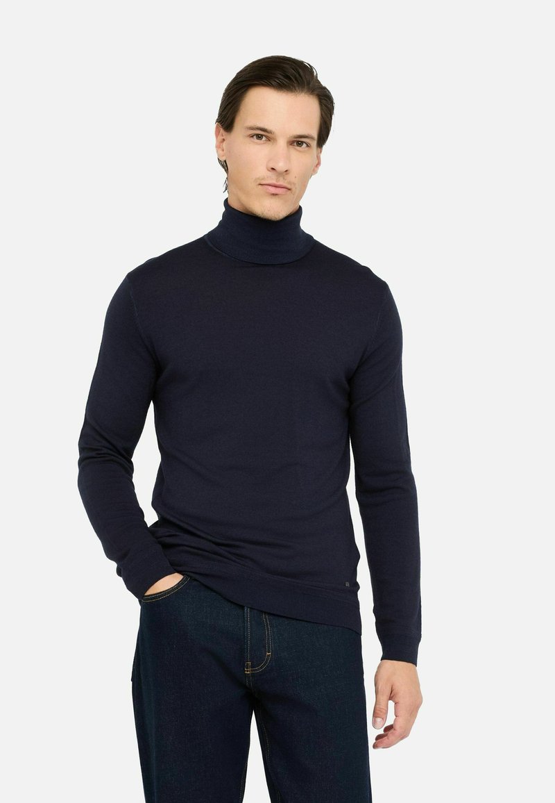Maglione a collo alto blu navy in un morbido tessuto lavorato a maglia, con maniche lunghe e polsini a costine, abbinato a jeans in denim scuro.