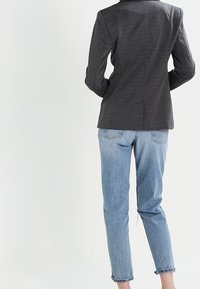 Blazer grigio dal design aderente, abbinato a jeans azzurri chiari. I jeans sono leggermente arrotolati ai polsini, creando un look casual.