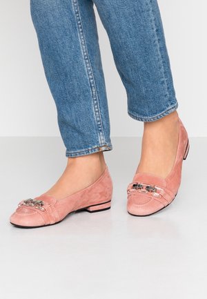 Lyserøde ruskinds flade sko med en rund tå, der har dekorative metalliske detaljer og syninger, placeret på en lav sort hæl.
