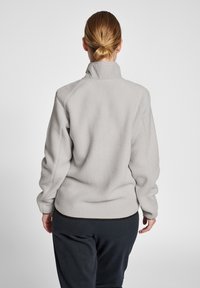 Ljusgrå fleece-pully med hög krage, raglanärmar och texturerad yta. Har en kontrasterande midja och ärmslut.