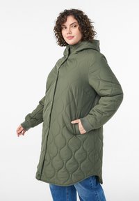 Zaļa dūnu jaka ar kapuci, aiztaisāma ar spiedpogām, ar sānu kabatām un ribotām aprocēm. Gluda tekstūra ar viļņotu rakstu.