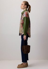 Mønstret patchwork skjorte med grønne læderærmer, mørkeblå jeans med frynset kant og en brun ruskinds håndtaske. Brune snørebåndsko.