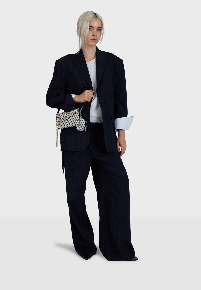Navy striped suit with oversized blazer and wide-leg trousers. White t-shirt underneath. Holds a patterned crossbody bag with chain strap.