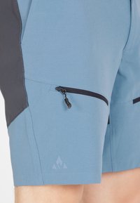 Ljusblå atletisk shorts med svart sidopanel, ficka med dragkedja och logotypdetalj ovanför fållen. Tillverkad av ett slätt, texturerat tyg.