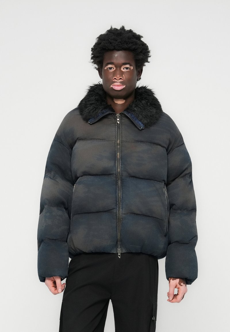 Blue puffer jacket with a fur collar, featuring a zip front, boxy shape, and quilted design. The fabric has a subtle texture and pattern.