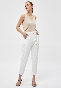 Light beige sleeveless top with a v-neck, paired with high-waisted white trousers featuring pockets, slim fit, and cuffed hems. Black strappy heels.