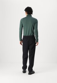 Groene gebreide coltrui gecombineerd met zwarte broeken met elastische taille. De broeken hebben zijzakken. Glad textuur, ontspannen pasvorm.