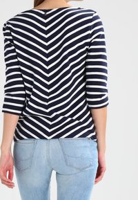 Marinblå och vit randig långärmad topp med en V-formad bakseam; kombinerad med ljusblå jeans med bakfickor och en figursydd design.