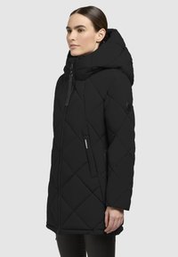 Must mustriga parka kõrge kraega ja suurte kapuutsiga, millel on esine tõmblukk, kaks küljetaskut ja logopatch varrukal.