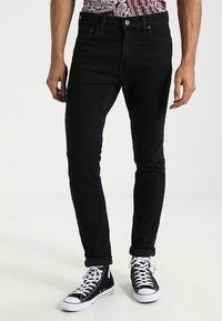 Czarne dżinsy o dopasowanym kroju, pięć kieszeni i podwinięte nogawki na kostkach, w zestawieniu z czarno-białymi sneakersami typu high-top.