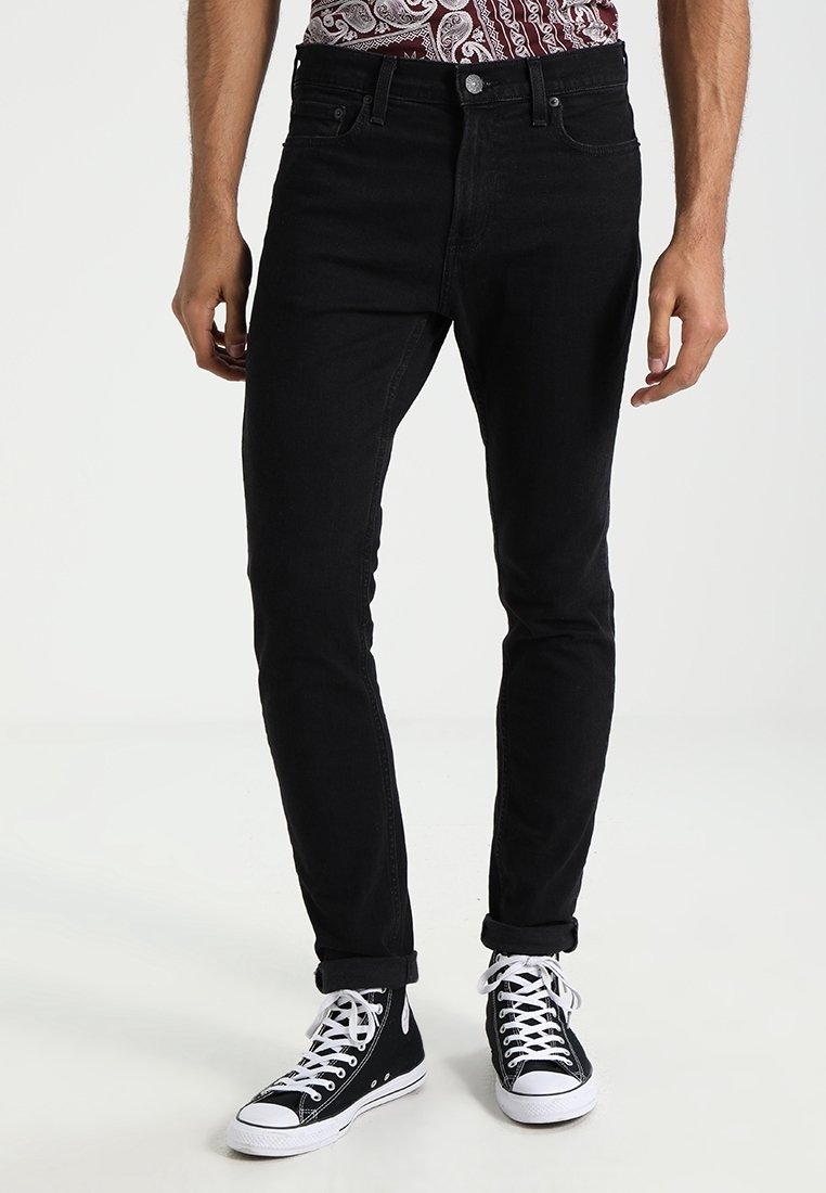 Czarne dżinsy o dopasowanym kroju, pięć kieszeni i podwinięte nogawki na kostkach, w zestawieniu z czarno-białymi sneakersami typu high-top.