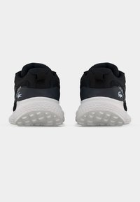 Ζευγάρι μαύρα sneakers Lacoste με λευκές σόλες, φαίνονται από πίσω, δείχνοντας υφασμένες εξωτερικές σόλες και λογότυπα της μάρκας στις φτέρνες.