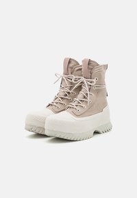 Bottes montantes beige clair avec un dessus en tissu texturé, embout en caoutchouc blanc et semelle en caoutchouc épaisse présentant un motif strié.