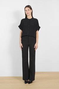 Camicia nera a maniche corte con bottoni e vestibilità morbida, abbinata a pantaloni neri a vita alta su misura e décolleté neri appuntiti.
