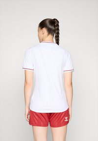 Valge spordisärk punase ääristusega, lühikeste varrukatega ja ümarate kraeäärega, sobitatud punaste pükstega, mille allääres on logo.